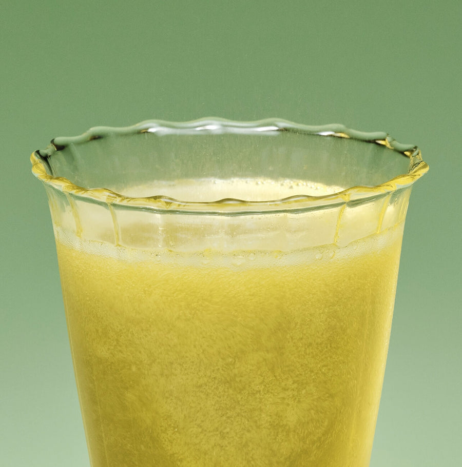 Glass of yellow liquid against a green background