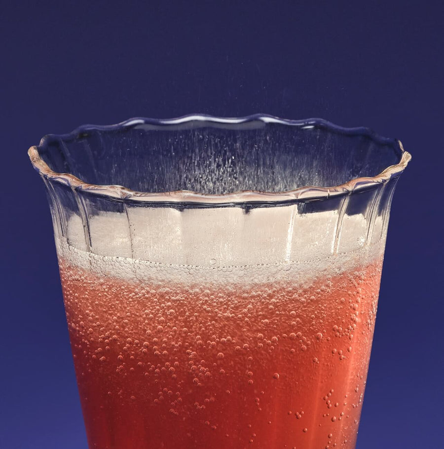 Clear glass with a red beverage against a blue background