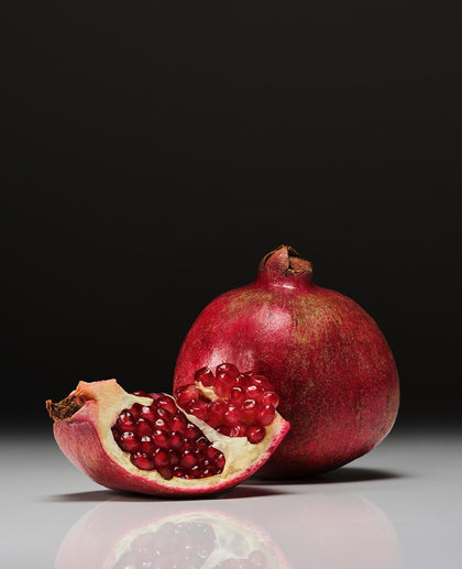 Pomegranate with a cut half on a reflective surface against a dark background