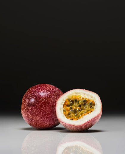 Passion fruit with one half sliced open on a reflective surface with a black background