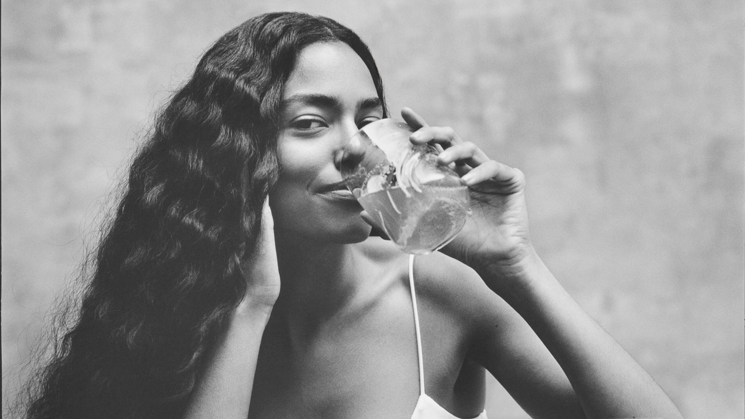 Black and white photo of a woman holding a glass with a drink against a neutral background