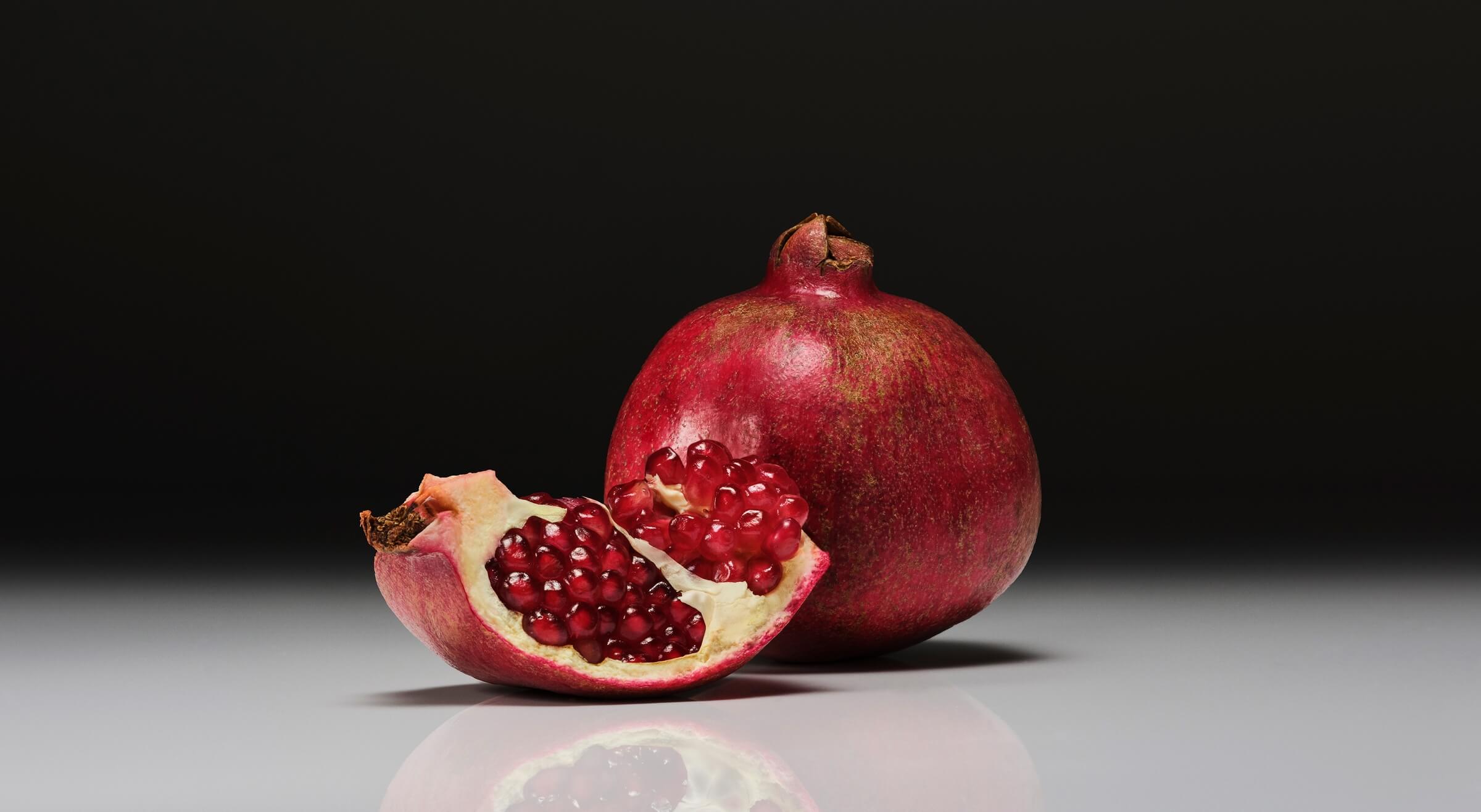 Pomegranate and a sliced pomegranate on a reflective surface with a dark background