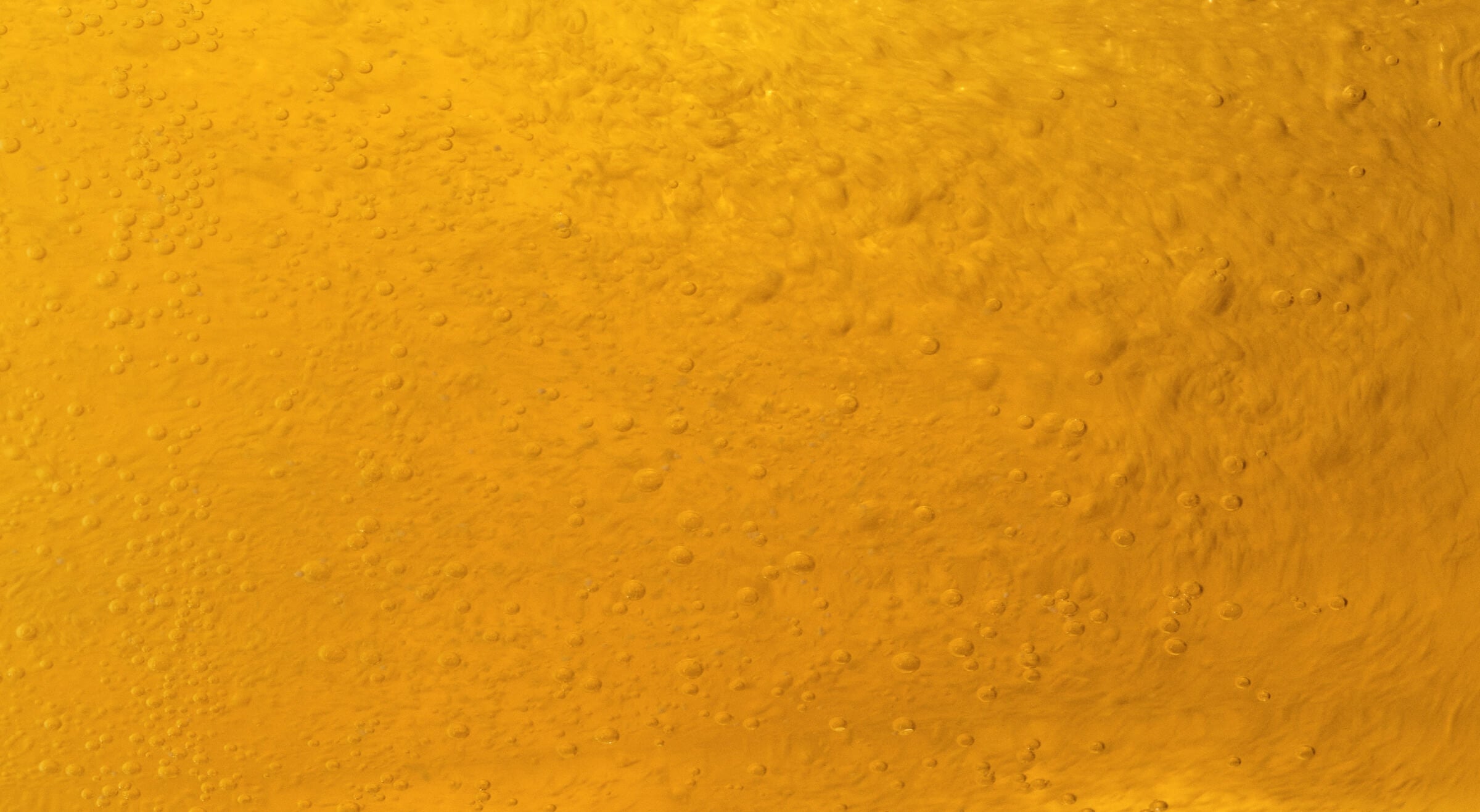 Close-up of golden yellow liquid with bubbles rising through it.