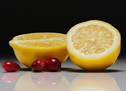 Two lemons, one whole and one halved, with cranberries on a reflective surface.