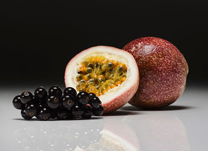 Passion fruit cut open with black currant  on a reflective surface