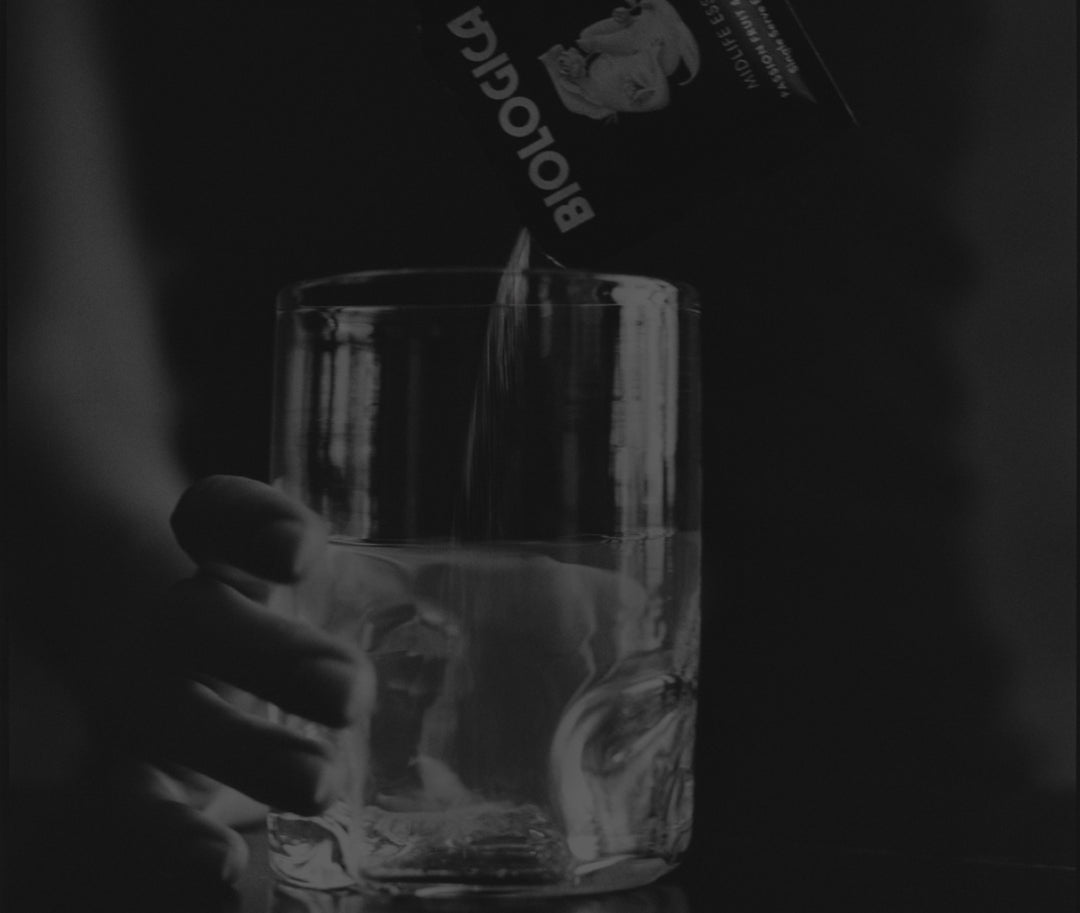 Hand pouring a clear liquid into a glass with a dark background