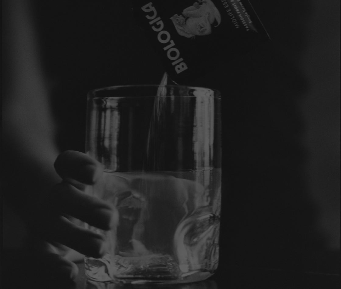 Hand pouring a clear liquid into a glass with a dark background