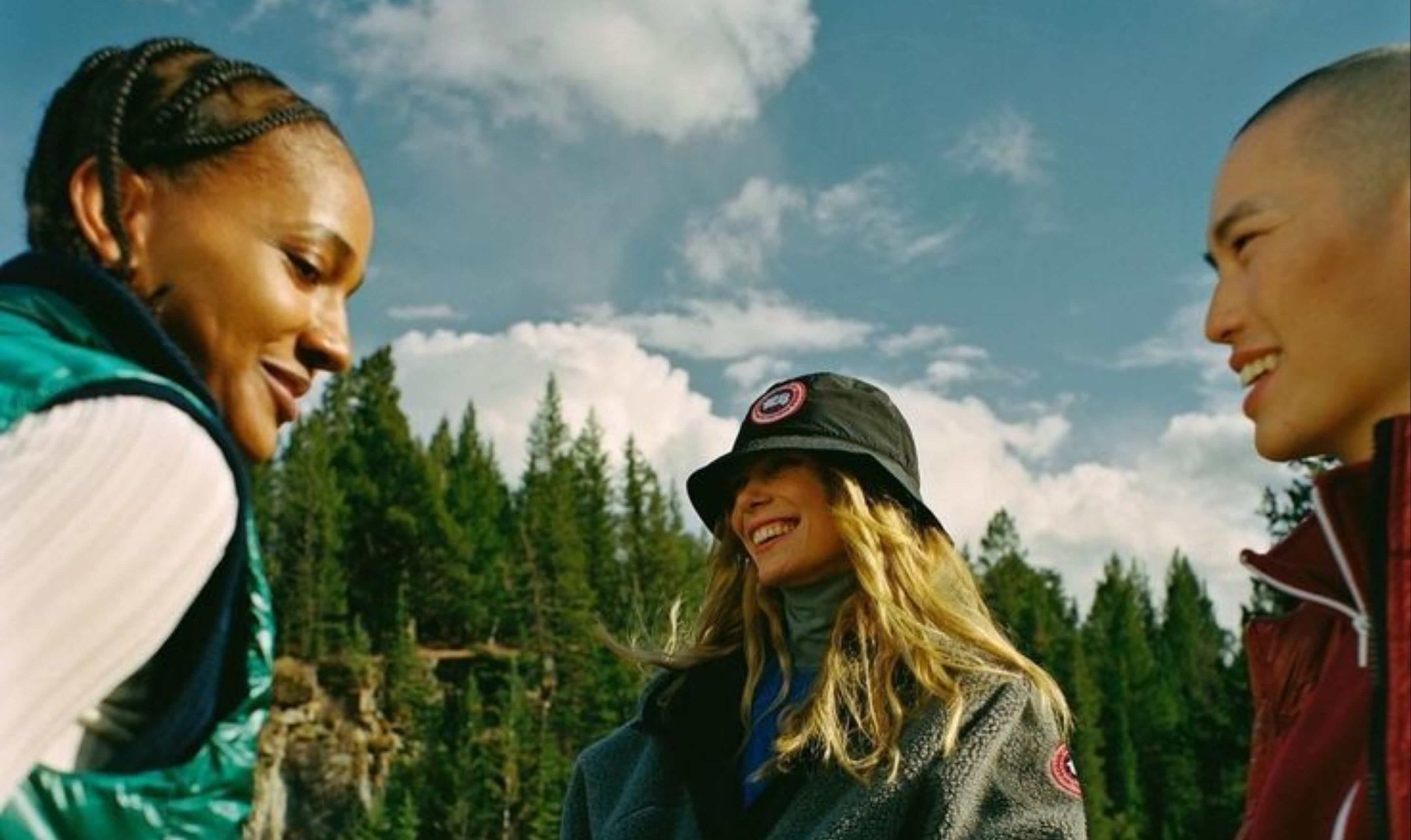 Three people standing outdoors with a forest and blue sky in the background