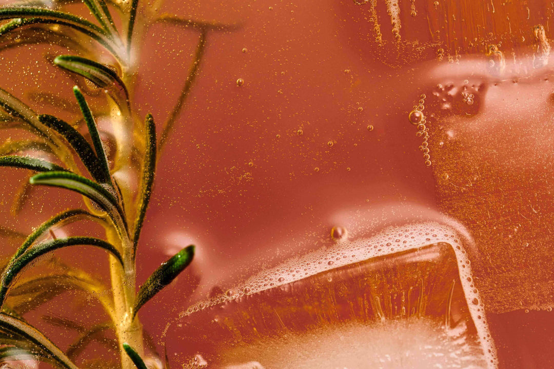 Close-up of a fizzy orange drink with ice cubes and a sprig of rosemary.